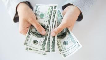 Two hands holding a bundle of of money and counting it.